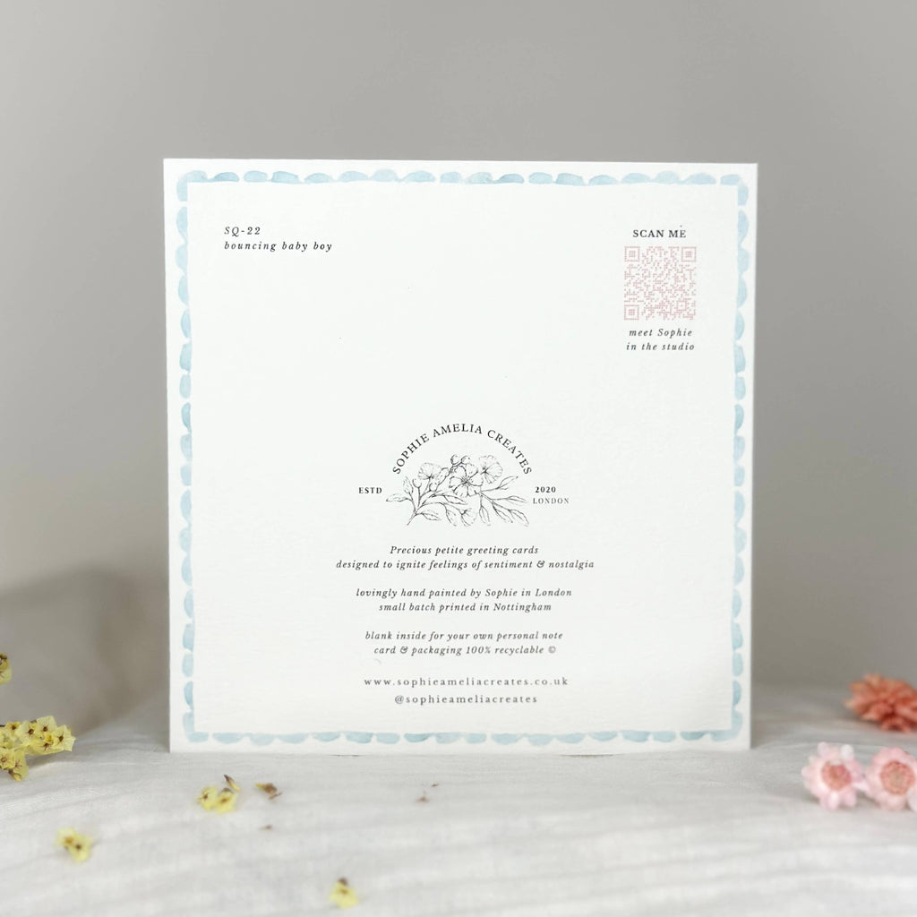 Baby shower invitation card on a gray surface with decorative flowers.