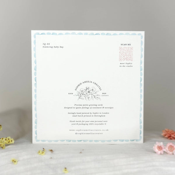 Baby shower invitation card on a gray surface with decorative flowers.