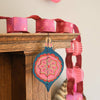 Decorative paper chain with pink and blue hanging ornaments on a wooden surface.