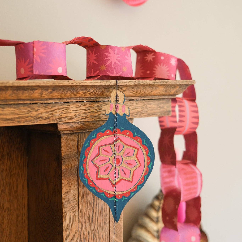 Decorative paper chain with pink and blue hanging ornaments on a wooden surface.