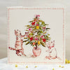 Card with illustration of two cats decorating a Christmas tree on a white surface.