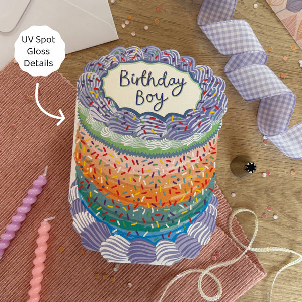 Colorful birthday cake card with 'Birthday Boy' text on a wooden surface.