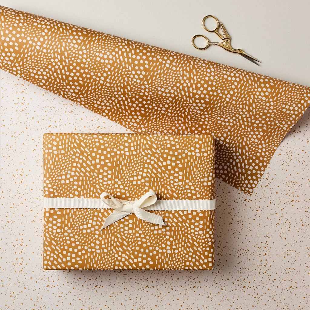 Gift box wrapped in brown patterned paper with a white ribbon, on a light speckled surface.