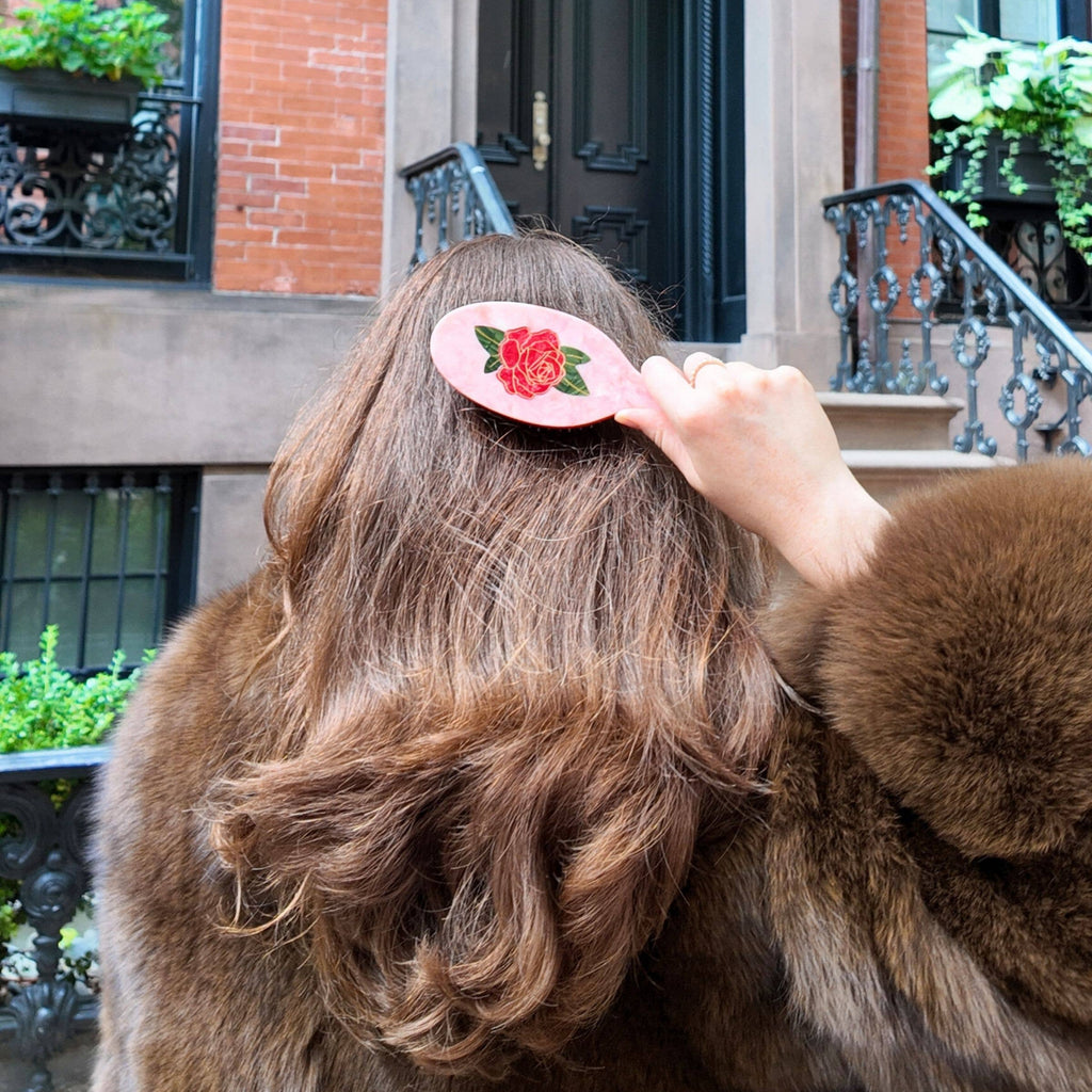 Person with a floral hair clip combing their hair outdoors.