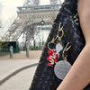 Person holding a black woven handbag with keychains in front of the Eiffel Tower.