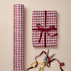 Red and white patterned gift wrap with a tied bow and gold scissors on a beige background