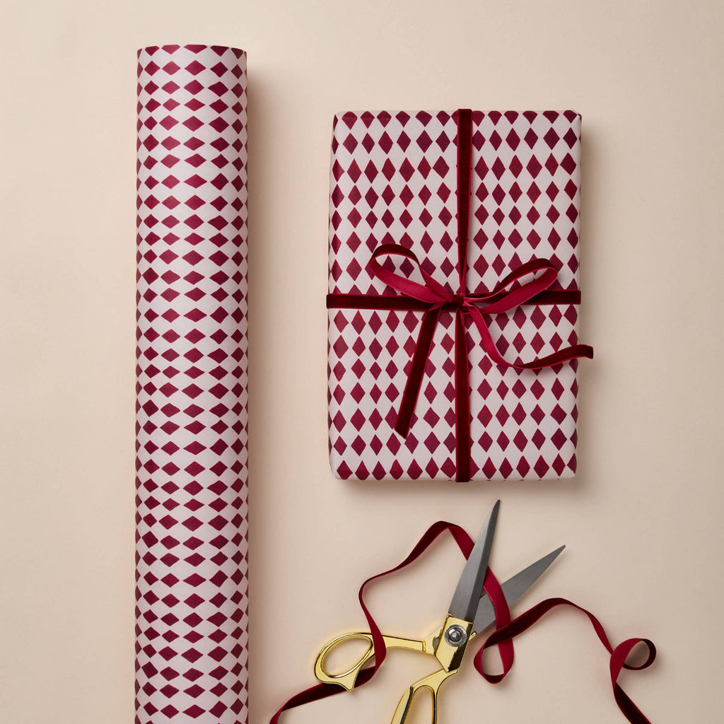 Red and white patterned gift wrap with a tied bow and gold scissors on a beige background