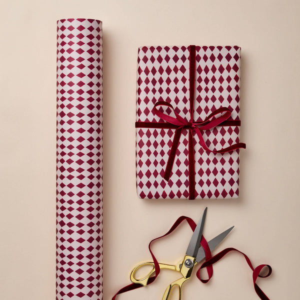 Red and white patterned gift wrap with a tied bow and gold scissors on a beige background