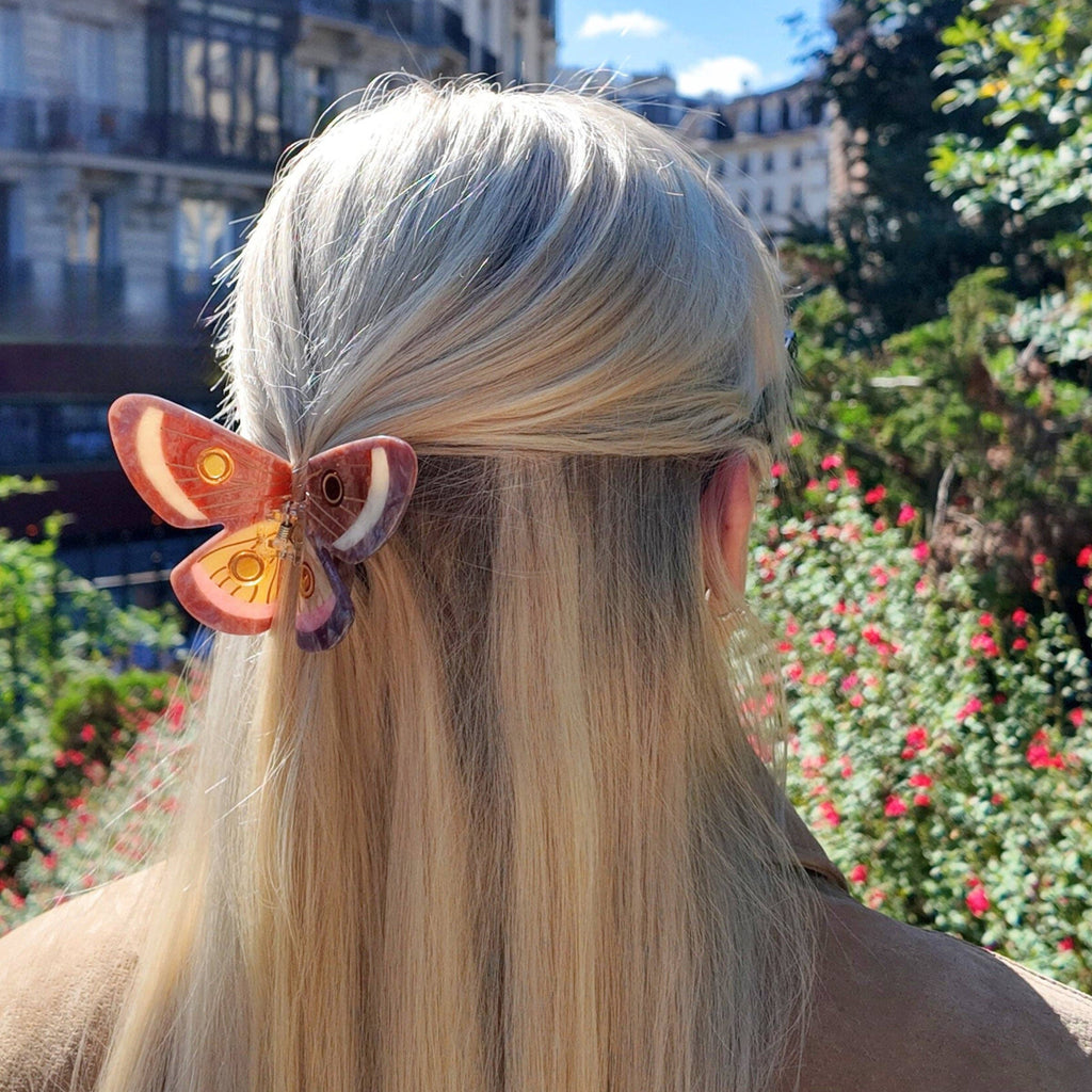 Person with long blonde hair wearing a butterfly hair clip in an outdoor setting