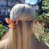 Person with long blonde hair wearing a butterfly hair clip in an outdoor setting