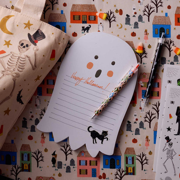 Ghost-shaped Halloween notepad with a pen on a patterned background