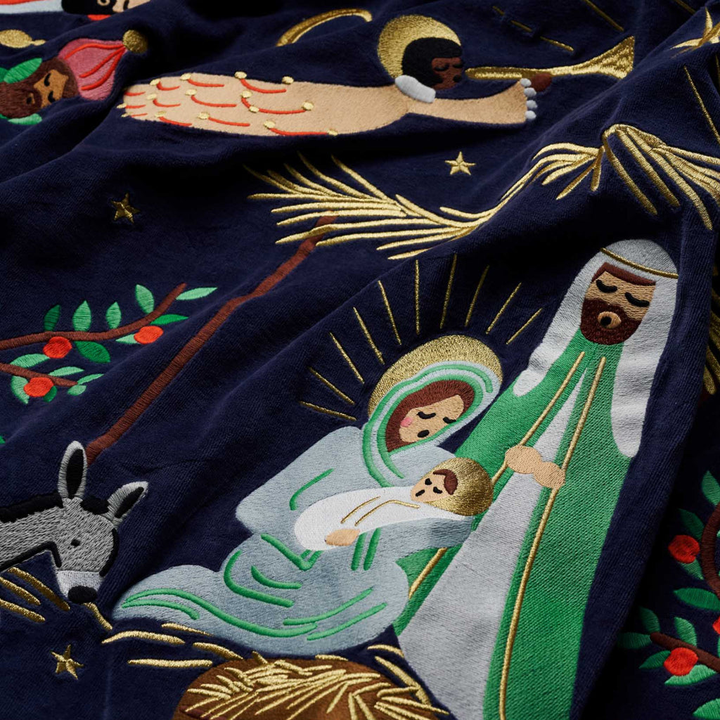 Embroidered nativity scene with Mary, Joseph, and baby Jesus on a dark blue fabric.