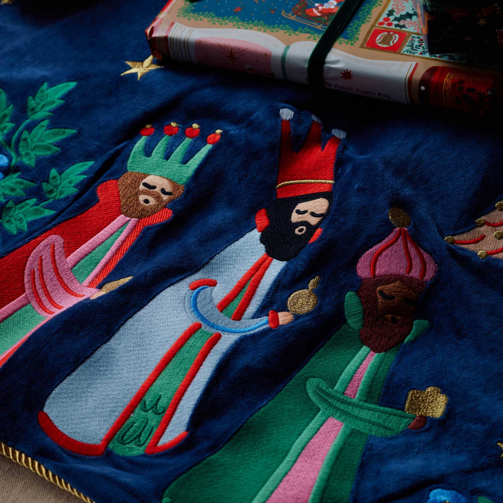 Embroidered design of three kings on a blue fabric with a book in the background.
