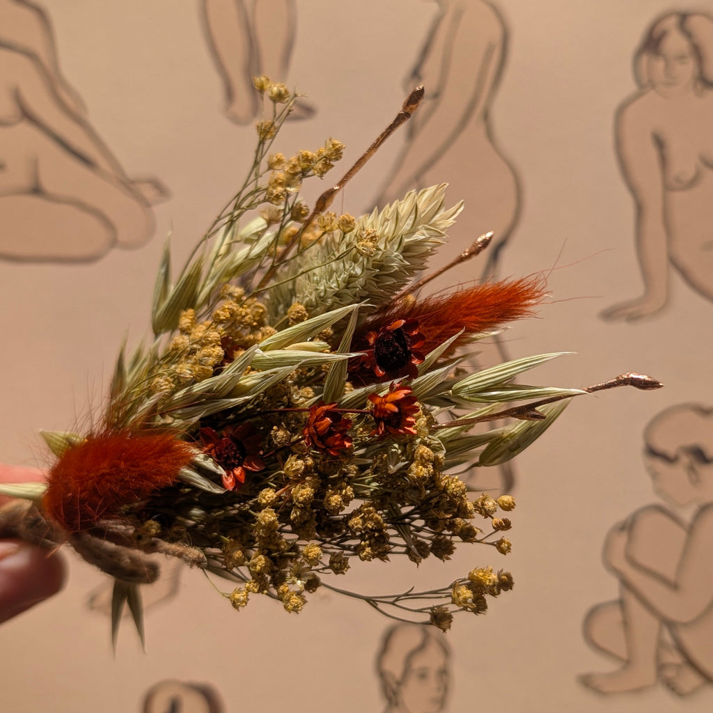 Dried floral arrangement held in front of a patterned background with human figures.